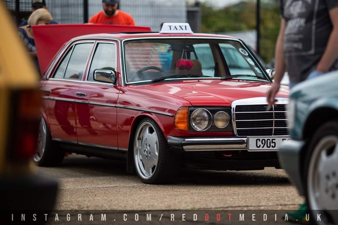 Red 1985 Mercedes-Benz W123 saloon on classic alloy wheels at a car show